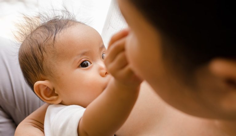 Mother breastfeeding her newborn baby beside window