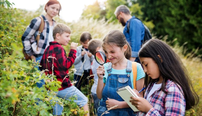 Group of school children with teacher on field trip in nature, learning science.